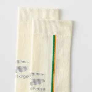Detail view of cream mid-tube athletic sports socks featuring green and orange stripes and logo.