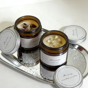 Detail shot of amber glass jar scented candles with dried rose and jasmine flower petals.
