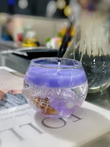 Detalle de cerca de vela aromática de gel morado con concha natural y perla.