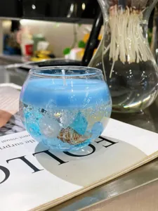 Vela aromática de cera gel azul en bol de vidrio redondo con concha perla y cristales.