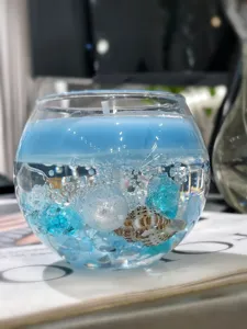 Vista detallada de la vela aromática estilo océano con conchas, perlas y cristales azules en vidrio.