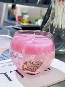Vela aromática de cera en gel rosa en cuenco de vidrio redondo con concha para decoración.