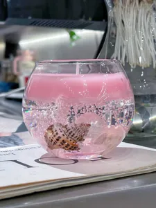 Vista detallada de una vela perfumada de gel con conchas y cristales en recipiente de vidrio.