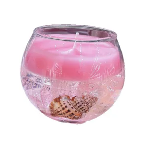 Vela aromática de vidrio redondo con cera rosa y decoración de concha para ambiente acogedor.