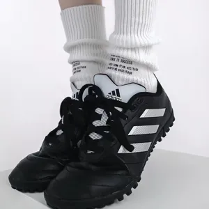 Detailed view of white ribbed knit crew socks with letter print, worn with sneakers.