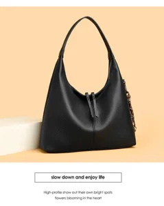Black leather hobo bag detail showing soft texture, zipper closure and side braided charm.