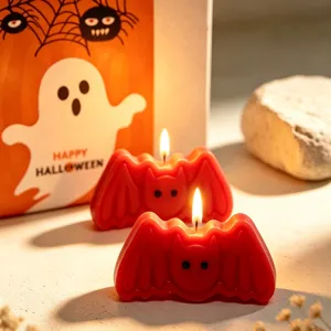 Detailed view of red bat shaped scented candles burning with warm glow for Halloween party decor.