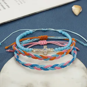 Dettaglio bracciali bohémien in filo di cera intrecciato con croce di strass e malocchio.