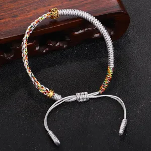 Dettaglio del bracciale tibetano intrecciato a mano con perlina dorata del mantra a sei sillabe