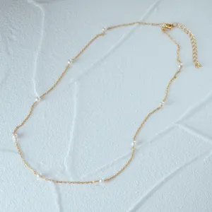Detailed view of a gold 925 silver necklace with elegant white pearls on white texture.