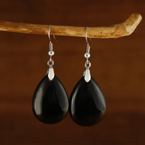 Primo piano di orecchini a pendente neri a goccia appesi a un ramo di legno naturale.