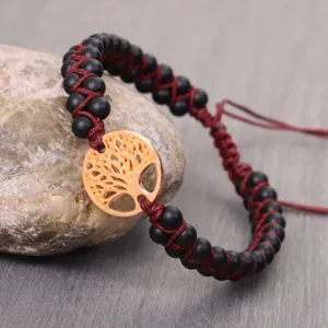 Close-up of handmade woven bracelet with matte black stone beads and golden tree of life charm