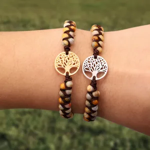 Nahaufnahme von zwei handgewebten Steinperlenarmbändern mit Lebensbaum-Anhängern in Gold.