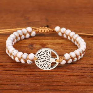 Detailopname van de levensboom-hanger aan een wit gevlochten yoga-armband met stenen kralen