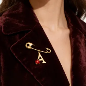 Detail view of a golden S925 silver safety pin brooch with a ladybug and letter A charm.