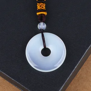 Detail eines lichtblauen Ping An Kou Anhängers an einer geflochtenen Schnur.