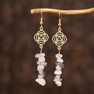 Détail de boucles d'oreilles yoga faites main avec symboles chakra dorés et pierres de cristal.