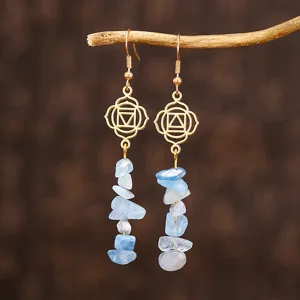 Détail de boucles d'oreilles pendantes en cristal bleu clair avec symboles de chakra yoga dorés.