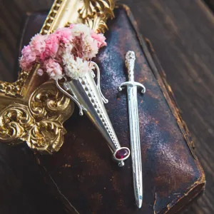 Close-up of vintage S925 silver vase and sword brooches with dried flowers on old book.