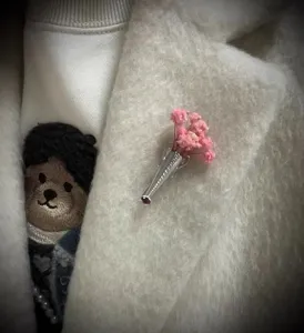 Detailed close-up view of a silver vase brooch with pink dried flowers on a white wool coat
