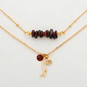 Detail of gold double-layer necklace with red garnet beads and snowdrop flower charm.