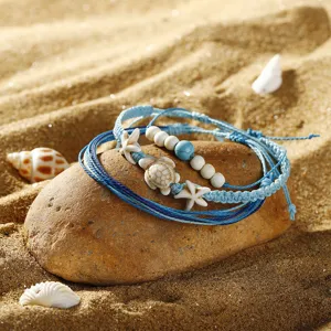 Detail von Boho-Armbändern mit Schildkröten- und Seesternanhängern auf feinem Strandsand
