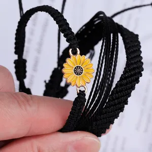 Detalle de una pulsera hecha a mano de cordón de cera trenzado negro con dije de girasol