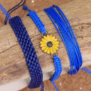 Detalle de set de pulseras bohemias tejidas a mano en azul con dije de girasol amarillo vivo.