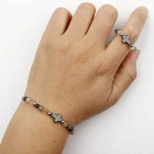 Detailansicht eines handgefertigten Perlenarmbands und Rings mit grauen Metallkreuz-Anhängern.