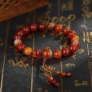 Macrodetail van een armband met rode agaat kralen en een decoratieve kwastknoop