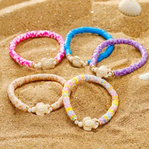 Nahaufnahme von böhmischen Heishi-Perlenarmbändern mit Schildkröten auf Sand.