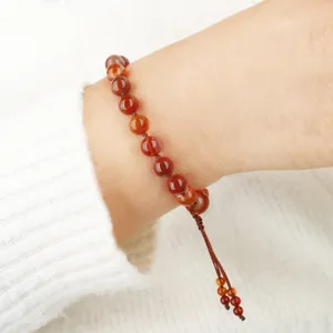 Close-up van een natuurlijke rode agaat kralenarmband gedragen om een pols met witte trui.