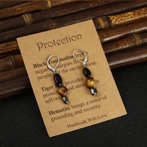 Primo piano di orecchini asimmetrici in pietra naturale con occhio di tigre ed ematite su card.