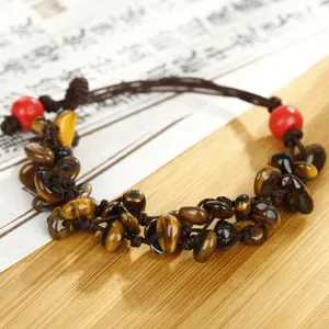 Bracciale intrecciato in pietra naturale occhio di tigre con perline rosse su stuoia di legno