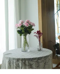 Artificial pink rose flower arrangement displayed in a clear glass vase on a lace tablecloth.