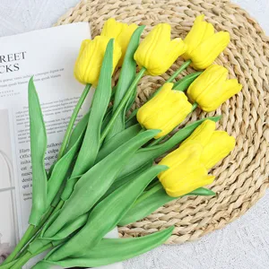 Detail shot of yellow artificial tulip bouquet with green leaves on straw mat background.
