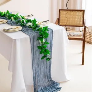 Détail de chemin de table en gaze froissée bleue avec guirlande de feuilles vertes pour déco.