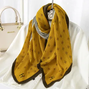 Detailed view of mustard yellow pleated scarf with brown contrast edges and H pattern.