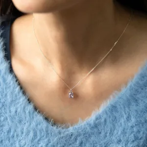 Gros plan d'un collier en argent délicat avec un pendentif carré en pierre violette éclatante.