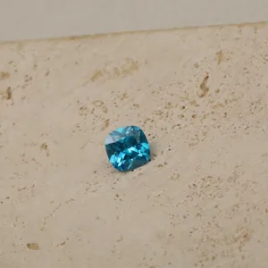 Close-up detail of a cushion-cut cyan cubic zirconia gemstone showcased on a textured stone surface