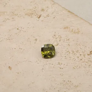 Macro view of a faceted cushion-cut olive green birthstone zircon on a textured stone surface.