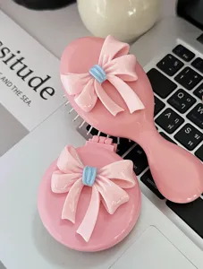 Detailed view of pink bow hairbrush and portable folding mirror massage comb set.