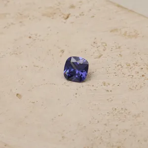 Macro detail of a sparkling purple cushion-cut zircon gemstone on a textured stone surface.