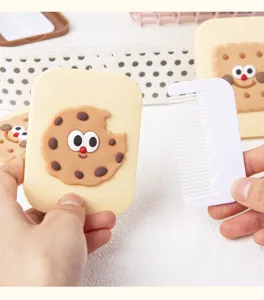 Primer plano del lindo espejo de maquillaje con forma de galleta y peine blanco