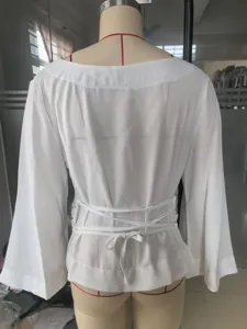 Back view detail of white boat-neck top with lace-up waist and flare bell sleeves.