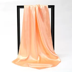 Detailed macro shot of a peach satin square scarf with elegant drape on white background