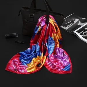 Detailed view of vibrant floral faux silk square scarf draped on a black leather handbag.
