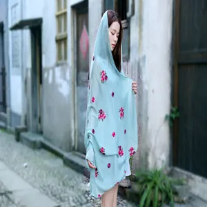 Detail of light blue linen scarf with pink floral embroidery worn as a sun protection shawl