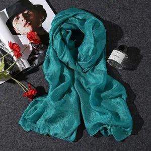 Detail view of a teal linen-cotton scarf with pearl luster on a textured background.