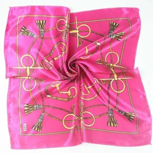 Detail of a bright magenta square scarf with golden equestrian chain patterns.